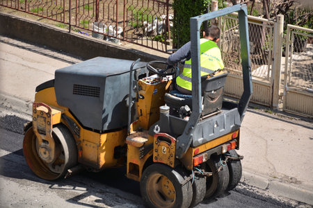 Nis, Serbia - April 24, 2021  Small road roller with worker rolling fresh hot asphalt on a city...