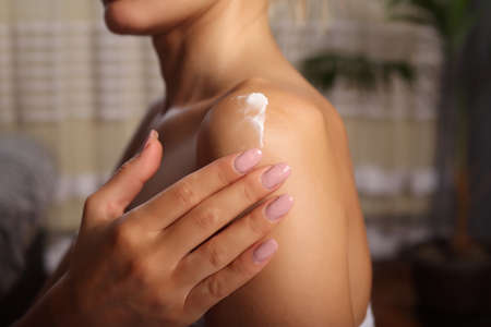 Woman with perfect skin in white towel applying cream on shoulder. Advertising of skin moisture and sunscreen product. Skincare and hydration conceptの写真素材