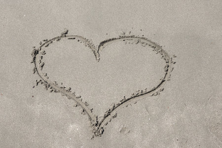 Hand drawing heart shape in the sea sand on the beach. Summer love concept. Close up, copy space for...