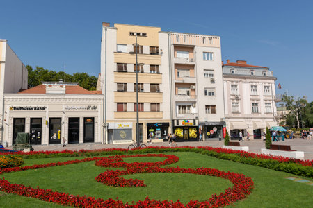 Nis, Serbia - August 14, 2021 Park with red flowers and old houses in downtown of Nis city on a...