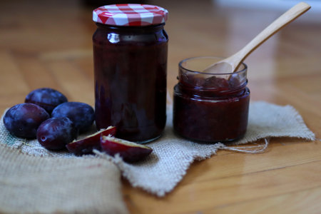 Glass jar with plum jam on a desk with fruit and retro background. Close up, selective focus and...