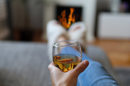 Female hand holding a glass of wine and lies in bed and relaxing next to the fireplace on a cold winter dayの写真素材