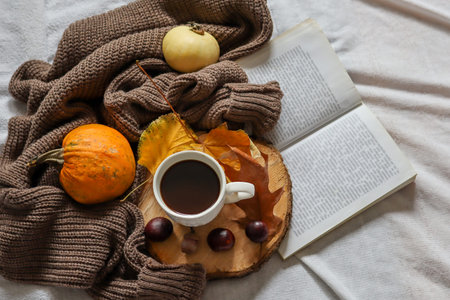 Autumn decorated background with coffee cup and book in bed. Close up, selective focus