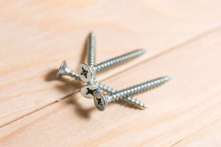 Group of metal screws on a wooden plank in carpenters workshop. Close up, selective focus, and copy spaceの写真素材