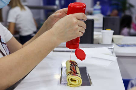 Pastry chef hands pour red strawberry syrup on pancakes in a restaurant. Fast food concept. Close up, selective focusの写真素材