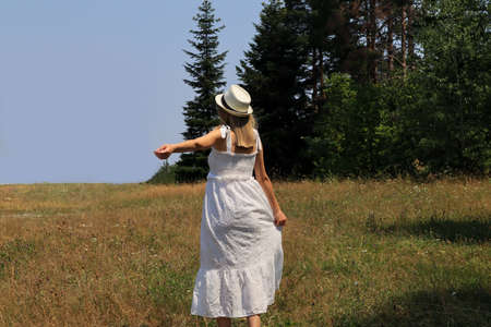 Woman in an elegant white dress and hat on her head enjoying beautiful nature on a hot summer day. Relaxation and enjoying the conceptの写真素材