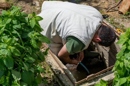 Man in a manhole releasing water for garden irrigation on a spring day in the countryside