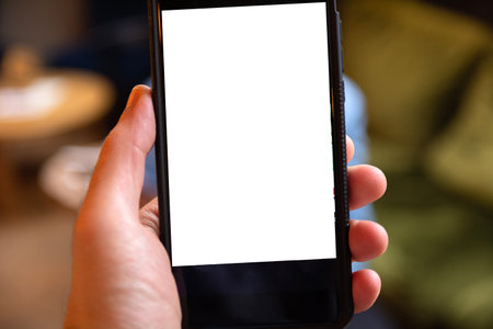 Close-up of a hand holding a mobile phone with a blank white screen for text or custom content. Blurred backgroundの写真素材