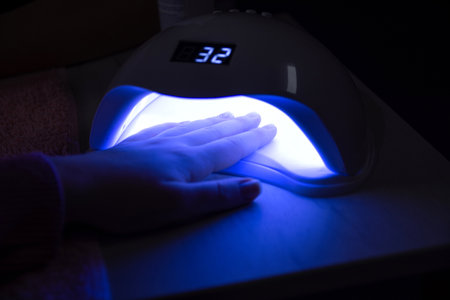 Close-up of a womans hand under a UV lamp for curing gel nails in a beauty salon, on a table. Manicure conceptの写真素材