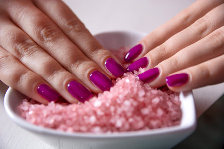 Close-up of female fingers with purple nail polish in a dish filled with sea salt, concept of manicure and nail careの写真素材