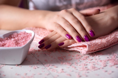 Female hands with purple nail polish on a towel and decorated white table in a studio, concept of manicure and feminine beautyの写真素材