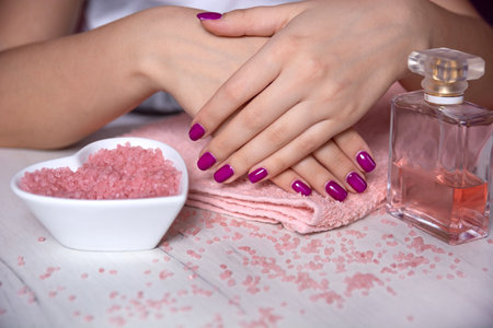 Purple manicure on delicate female hands on a pink towel and decorated table in a studio, concept of manicure, fashion, and beautyの写真素材