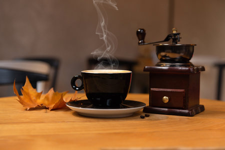 Coffee cup and coffee grinder on a wooden desk with autumn dry leaf in a bar. Drink concept. Copy space for design or textの写真素材