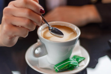 Female hand stirring coffee with a small metal spoon on a restaurant desk. Drink concept, close-up, selective focus.の写真素材