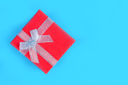 Red gift box with a tied ribbon on a classic blue background in a studio. Christmas or Valentine's Day concept with copy space for text or designの写真素材