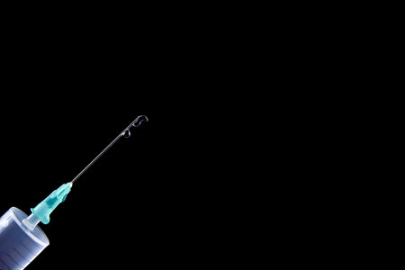 Syringe with a drug injection drop isolated on a black background. Health and medical concept with copy space for text or design, close-up, selective focusの写真素材