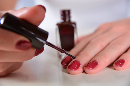 Close-up of a woman applying red nail polish with a brush on a white desk. Manicure and beauty conceptの写真素材