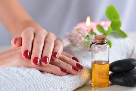 Close-up of female hands with red nail polish on a towel in a beauty studio. White desk with decorative elements. Manicure conceptの写真素材