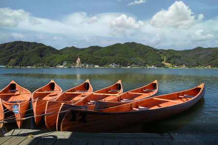 Canoes sit in the water of a river in summer in panorama view. Canoes rest on a bank of a lake, mountains in background.の写真素材