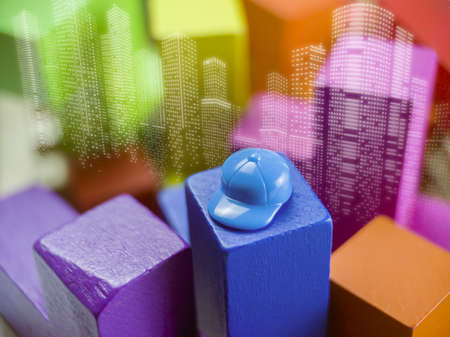 Colorful wooden building blocks with a blue helmet on the background of the cityの写真素材