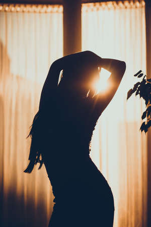 Silhouette of a girl, not in focus, on the beach during sunset. Woman exercising stretching, gymnastic exercise, practicing yoga. On the background summer dark landscape. Concept of sport lifestyle.の写真素材