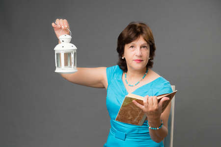 Mature student woman with book and lantern on dark backgroundの写真素材