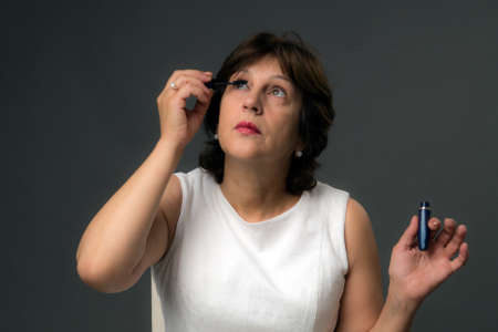 Attractive Mature Woman in White Dress Applying Mascaraの写真素材