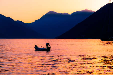 Fisherman silhouette at sunset in sea on mountain background in Kotor Bay Montenegroの写真素材