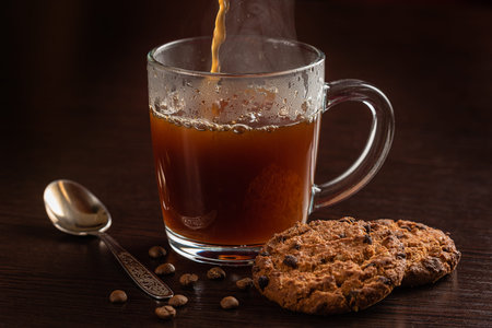 a hot drink fills the Cup. oatmeal cookies lie on a wooden table nearby. horizontal studio...