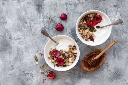 Two bowls with yogurt, honey, muesli and cherries on stone background. Fresh yogurt. Healthy food concept. Top view, copy spaceの写真素材