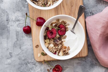 Two bowls with yogurt, honey, muesli and cherries on stone background. Fresh yogurt. Healthy food concept. Top view, copy spaceの写真素材
