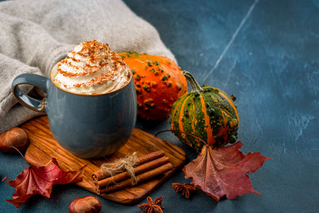 Pumpkin spice latte in a blue mug with whipped cream, cinnamon. Blue background decorated autumn leaves, pumkin.の写真素材