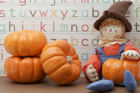 Smiling scarecrow sitting against Alphabet background holding pumpkinの写真素材