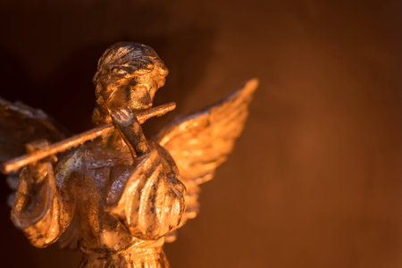 Winged angel playing the flute in warm light and gold tones.