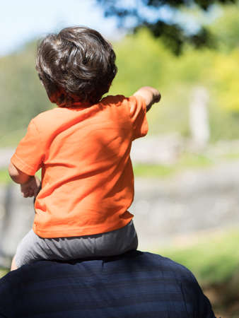 Toddler looks beyond while seated on dads shouldersの写真素材