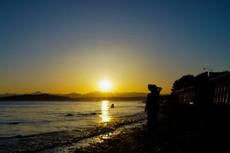 Female Walking Along Rocky Beach Enjoying View At Sundown Silhouetteの写真素材