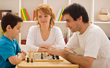 Father and his son playing chess meantime the young beautiful woman smilingの写真素材