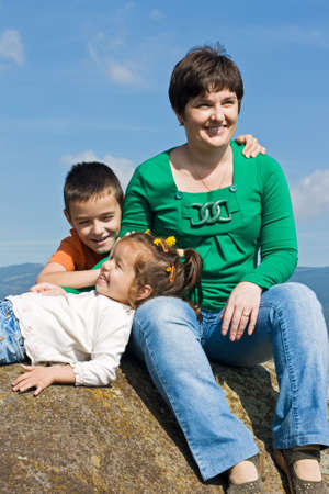 Beautiful woman and her happy children sitting on the stoneの写真素材