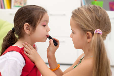 Little girl applying lipstick on her girlfriend's mouthの写真素材