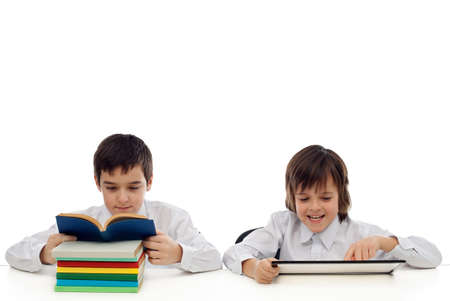 Two boys at the table, one of them reading traditional from the book the other playing on the tabletの写真素材