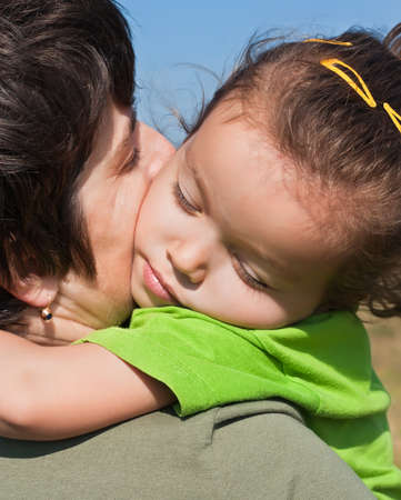 Little girl with closed eyes resting on her mother's shoulderの写真素材