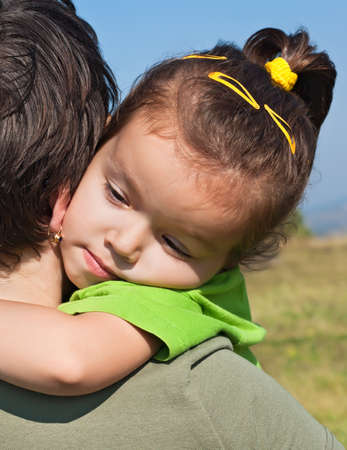 Happy little girl resting on her mother's shoulderの写真素材