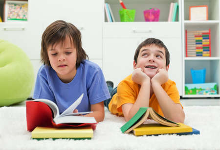 Two little boys with books, the one reading with  interest and the other dreaming looking up near the booksの写真素材