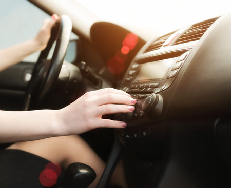 Woman in a car use audio system. Sunset shot with flares