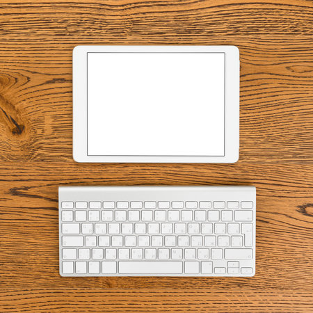 Modern tablet computer with blank display and keyboard on the desk of workplace. Top view.