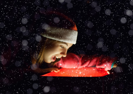 Little girl dressed as Santa Claus over red box with light with surprised face, black background and...