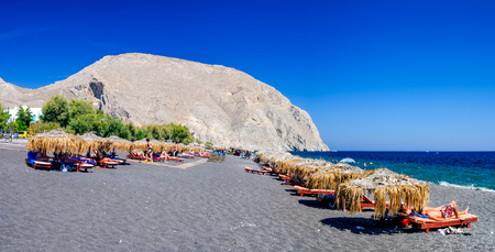SANTORINI GREECE  19 SEPTEMBER 2010: People sunbathing and swimming at black beach of Kamari in Santorini Greece. Beach is covered with fine black sand and drops off sharply into the water.のeditorial素材