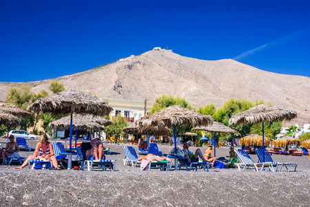 SANTORINI GREECE  19 SEPTEMBER 2010: People sunbathing and swimming at black beach of Kamari in Santorini Greece. Beach is covered with fine black sand and drops off sharply into the water.のeditorial素材
