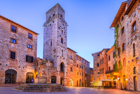 San Gimignano, Italy. Piazza della Cisterna with triangular shape, medieval hilltop city in Tuscany, twilight illuminated scene.の写真素材