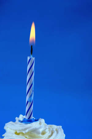 Birthday cupcake with a single candle on it on blue backgroundの写真素材